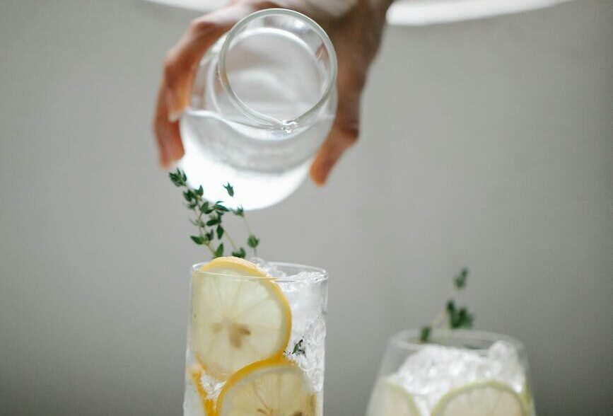 crop person pouring water into lemon drink