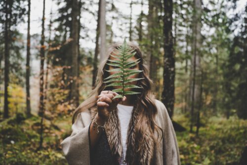 woman standing at woods holding green plant