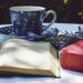 book opened on top of white table beside closed red book and round blue foliage ceramic cup on top of saucer