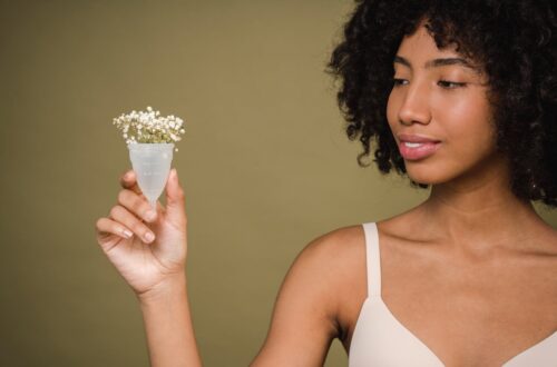 positive young black lady demonstrating menstrual cup in beige studio