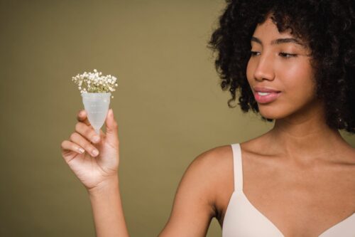 positive young black lady demonstrating menstrual cup in beige studio