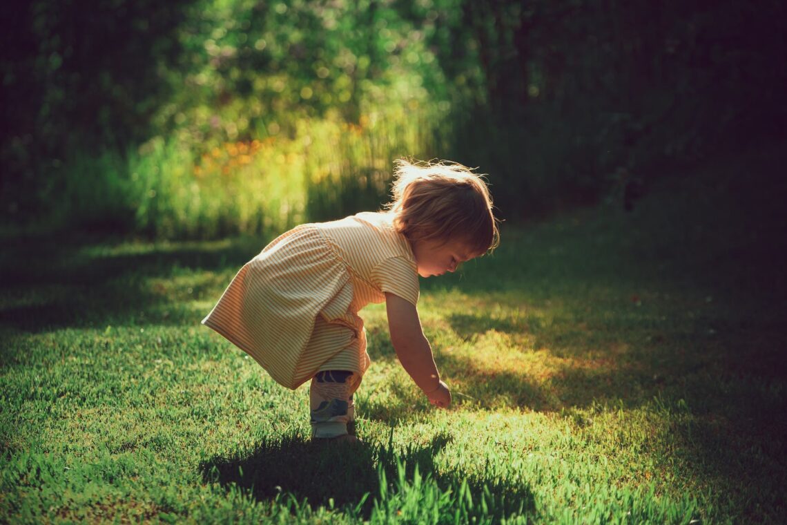 little girl playing with shadow on grass lawn in summer