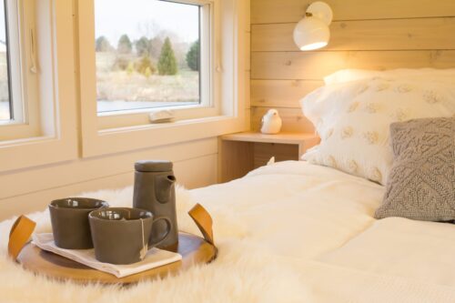 cups of tea on a wooden tray placed above the bed