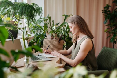 woman surrounded by indoor plants while writing on a notebook