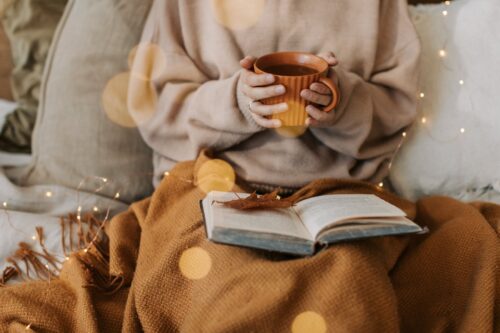 person in beige sweater holding a cup of warm beverage